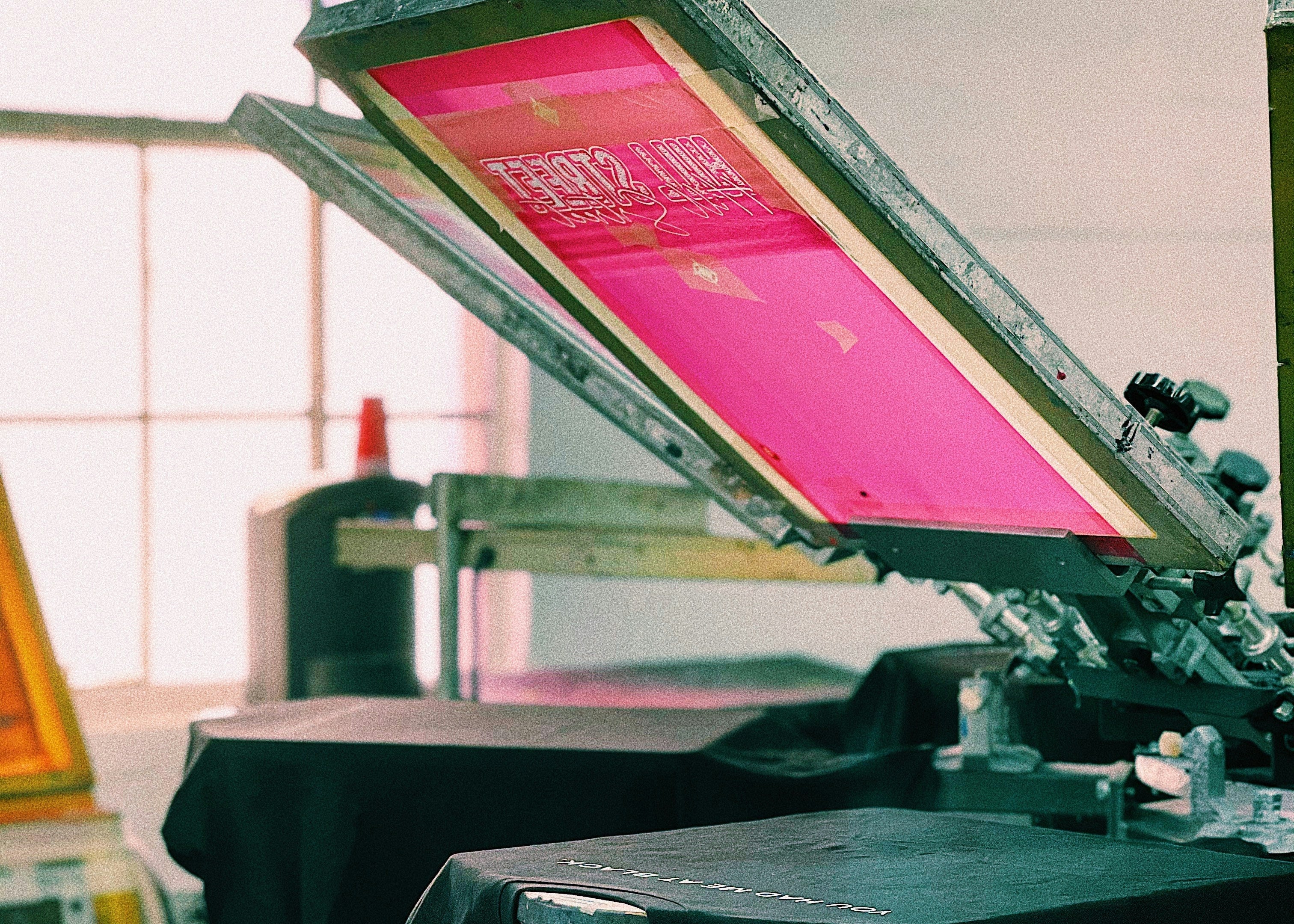 Screen printing press with pink ink on a black shirt in a studio setting